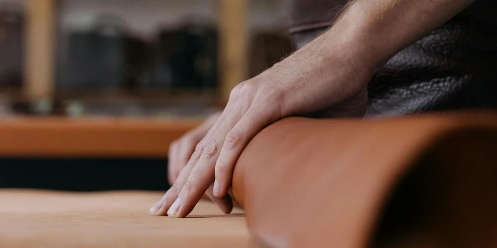Close-up of hands massaging and flexing a brown leather accessory to keep it supple.