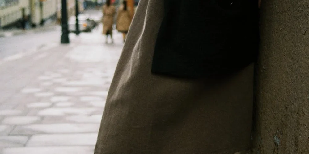 Urban street scene with a person leaning against a stone wall and pedestrians in the background.