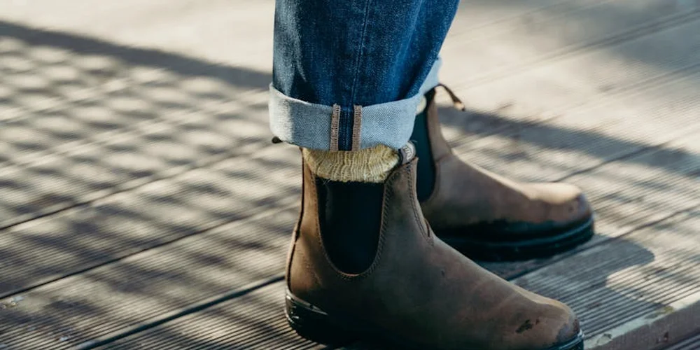 Brown leather ankle boots with rolled jeans standing on a wooden surface.