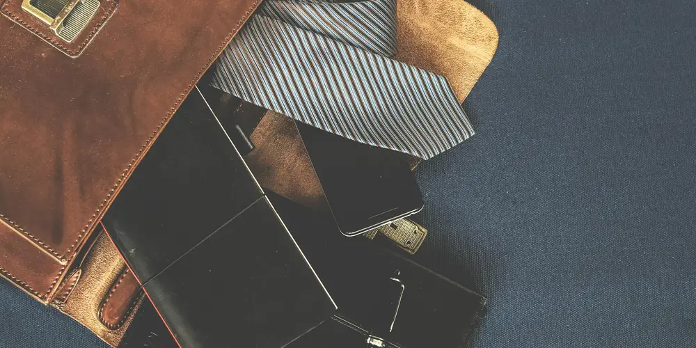 Close-up of various leather bags and accessories, showing textures and wear on brown leather with a striped fabric and a dark background