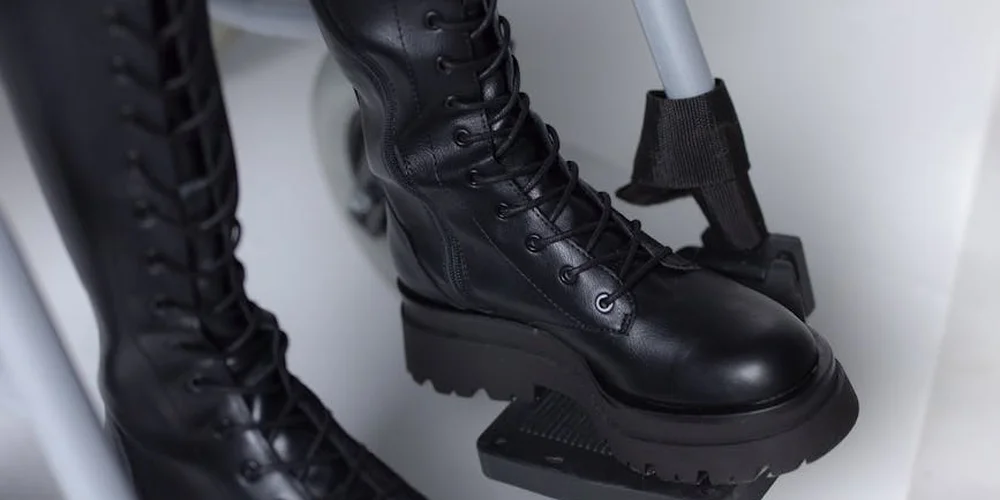 Close-up of black leather boots with laces and rugged soles, resting on a stand.