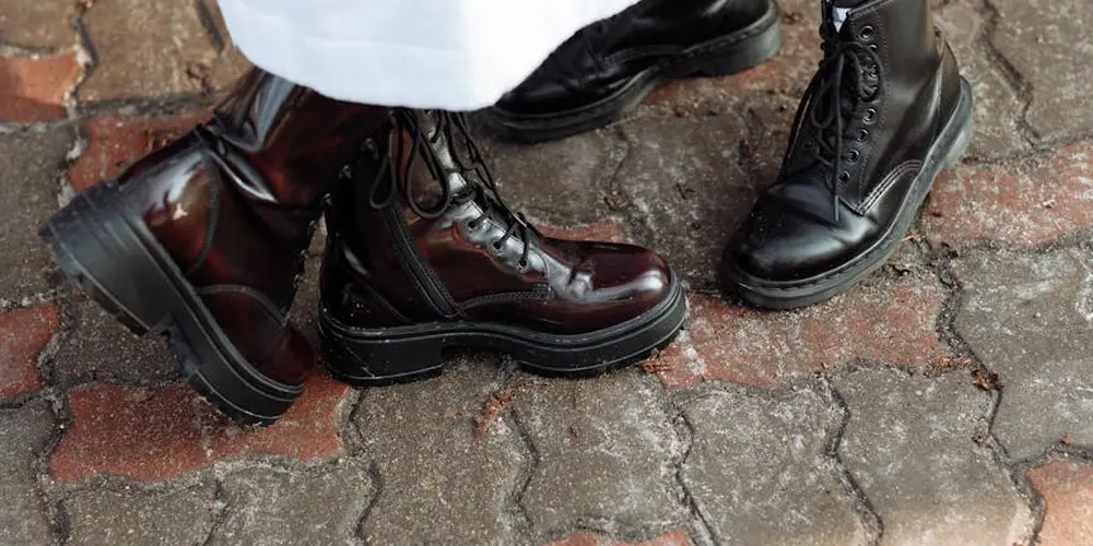 Close-up of dark leather boots resting on a brick pavement, with white fabric nearby