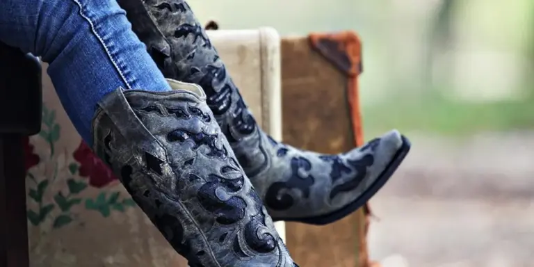 Pair of patterned leather boots resting outdoors with blue jeans visible, illustrating the break-in process.