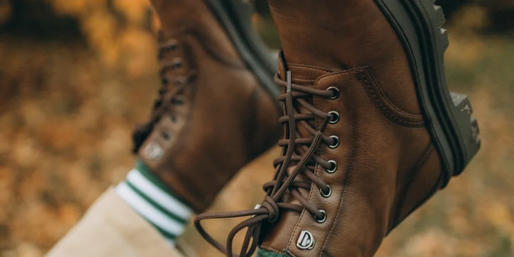 Brown leather lace-up boots with a rugged sole resting on a fall backdrop; a striped sock is visible above the boot.