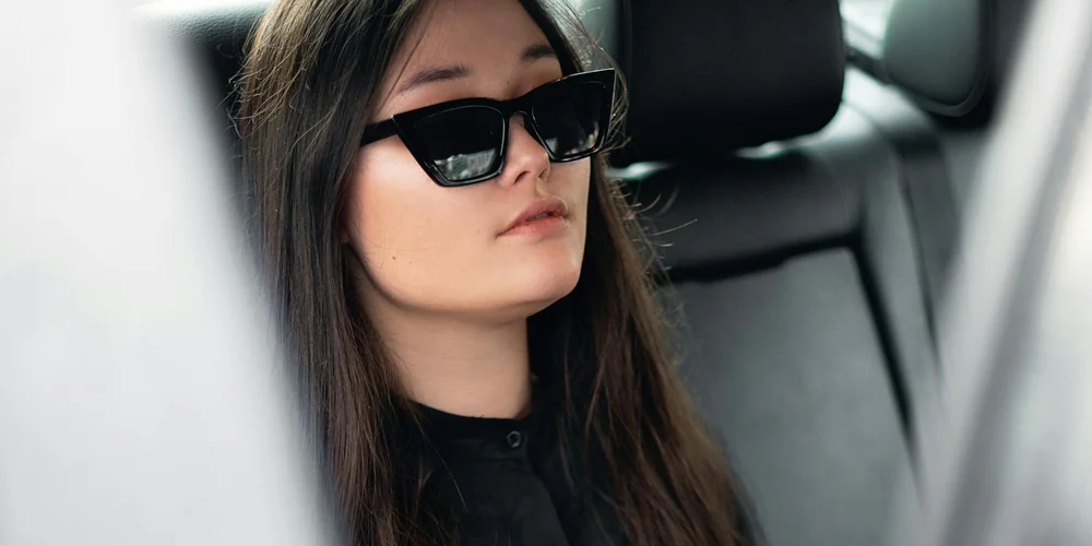 Person wearing sunglasses sits in the back seat of a car