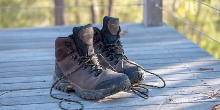 Pair of rugged leather hiking boots on a weathered wooden deck outdoors.
