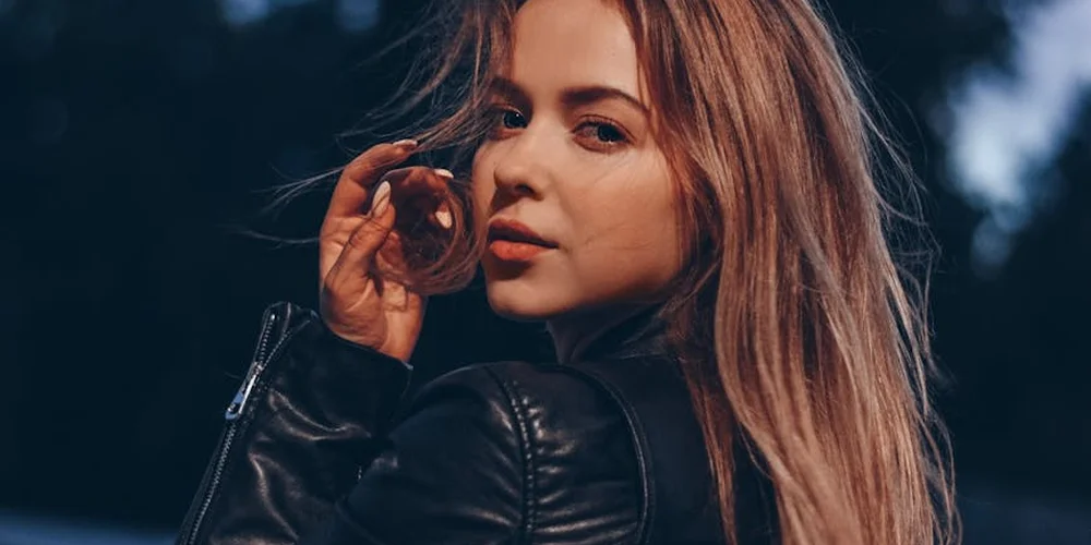A person wearing a black leather jacket outdoors, looking over their shoulder.