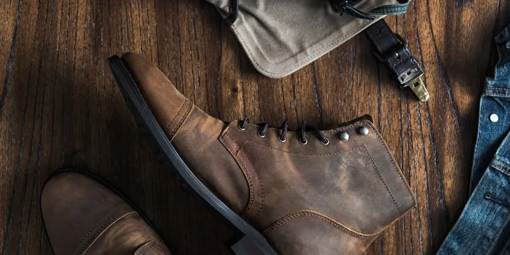 Brown leather boot on a wooden floor with a denim garment nearby, illustrating leather care.