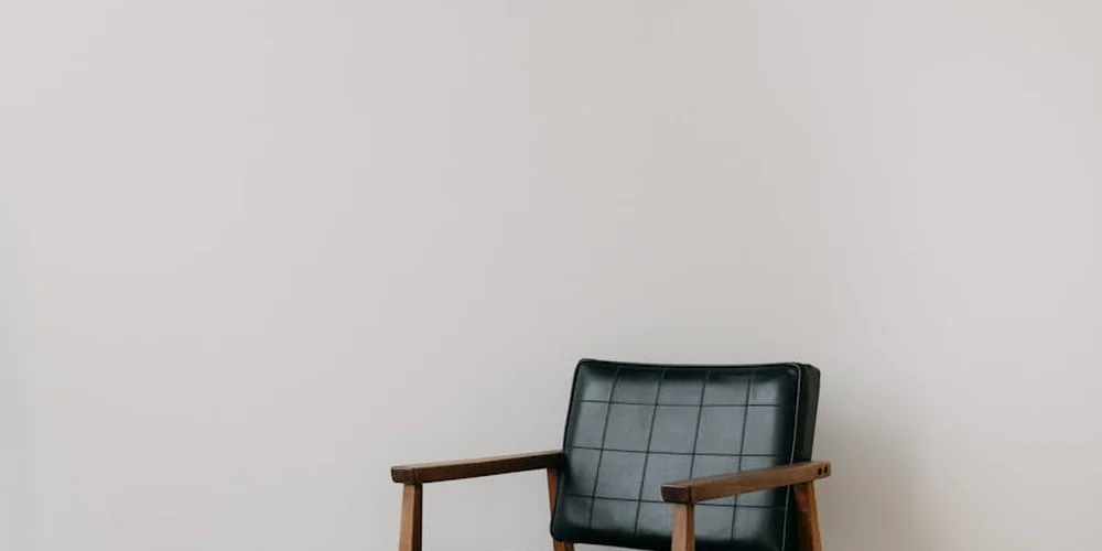 Black leather armchair with wooden arms against a light beige wall