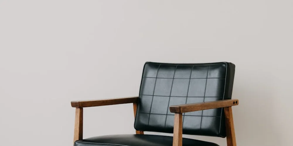 Black leather chair with wooden armrests against a light background.