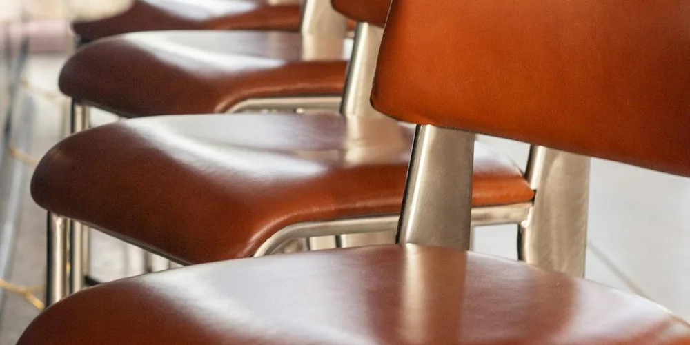 Close-up of smooth brown leather chairs in a row, highlighting the leather surface and stitching.