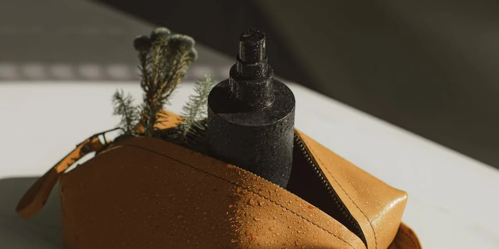 Close-up of a brown leather item on a white surface with a black spray bottle and a small plant sprig