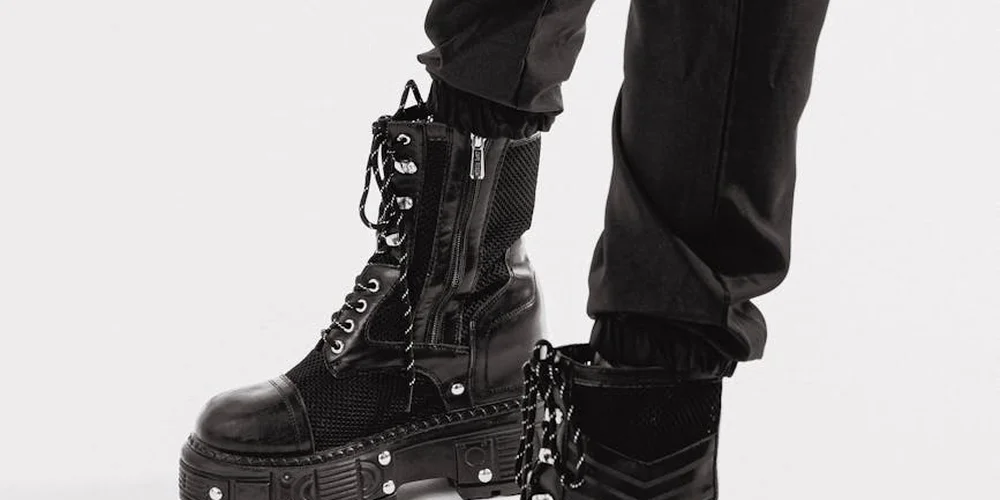 Close-up of black leather boots with laces and zippers, standing on a light background.