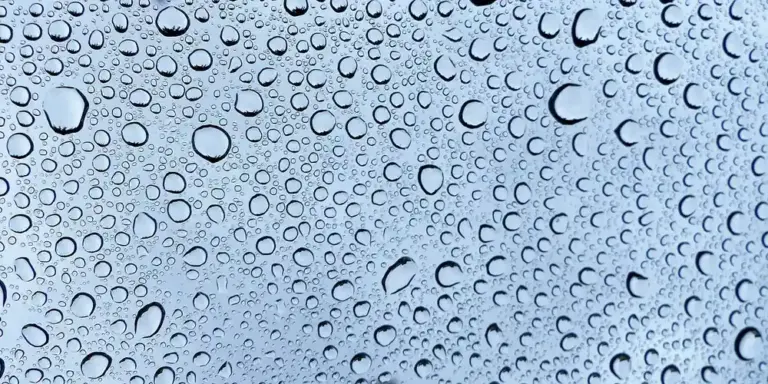 Close-up of numerous water droplets on a blue-tinted glass surface