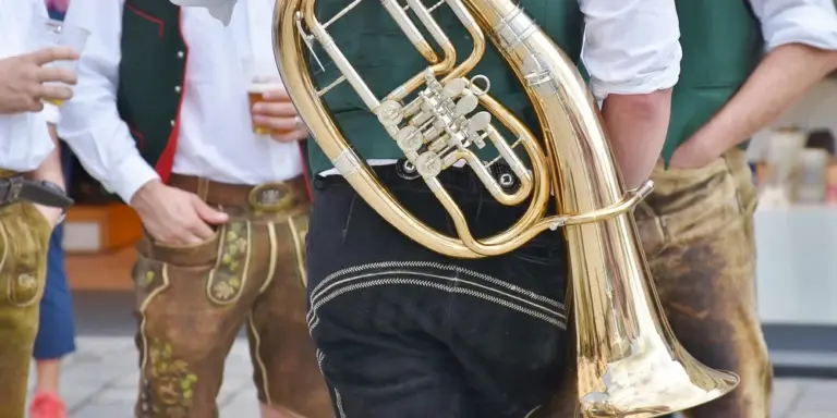 Group of people wearing traditional leather lederhosen indoors, with a brass instrument.