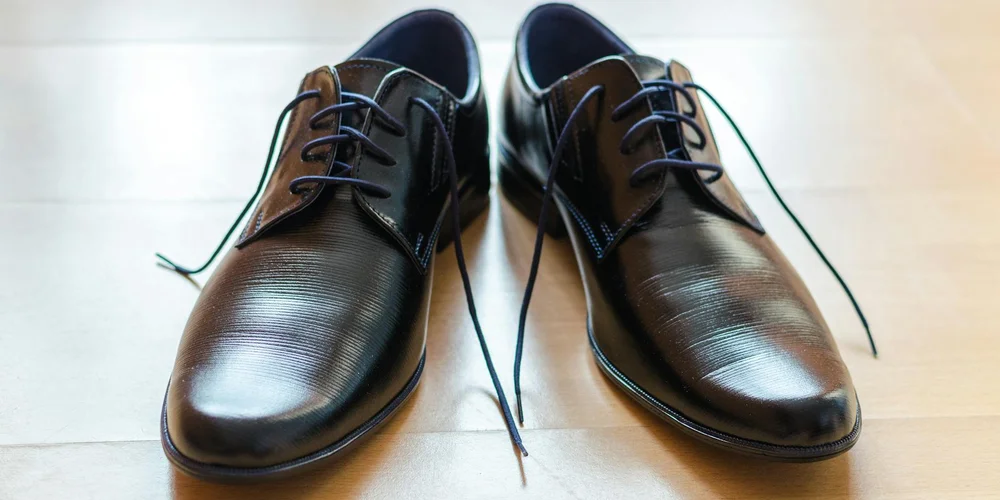 Brown leather dress shoes with laces resting on a light wooden floor