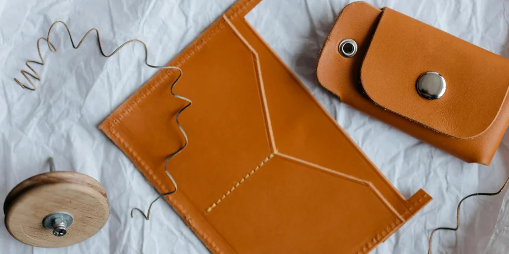 Brown leather pieces and a wooden thread spool on a white surface, with visible stitching and loose thread, illustrating leather embroidery and embellishment.
