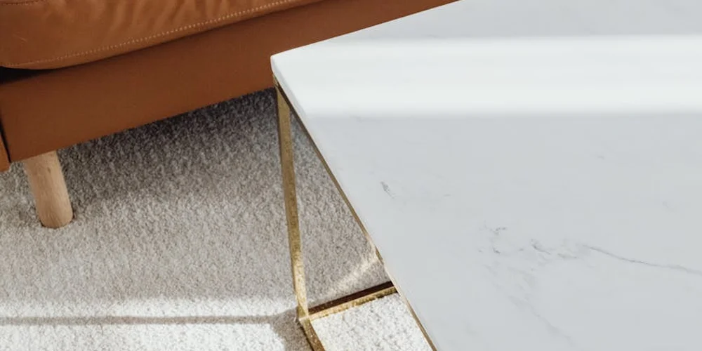 A brown leather sofa next to a white marble coffee table on a light carpet, illustrating a pristine setup aimed at preventing wrinkles in leather.