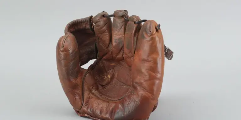 A well-worn brown leather glove resting on a light gray surface.