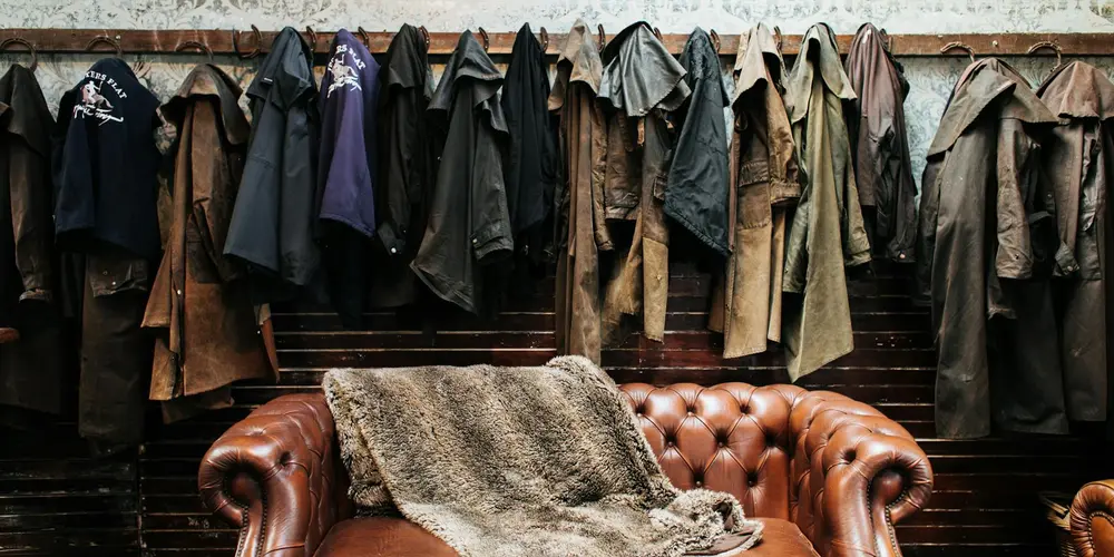 Brown tufted leather sofa with a draped fur throw, set against a backdrop of hanging jackets.
