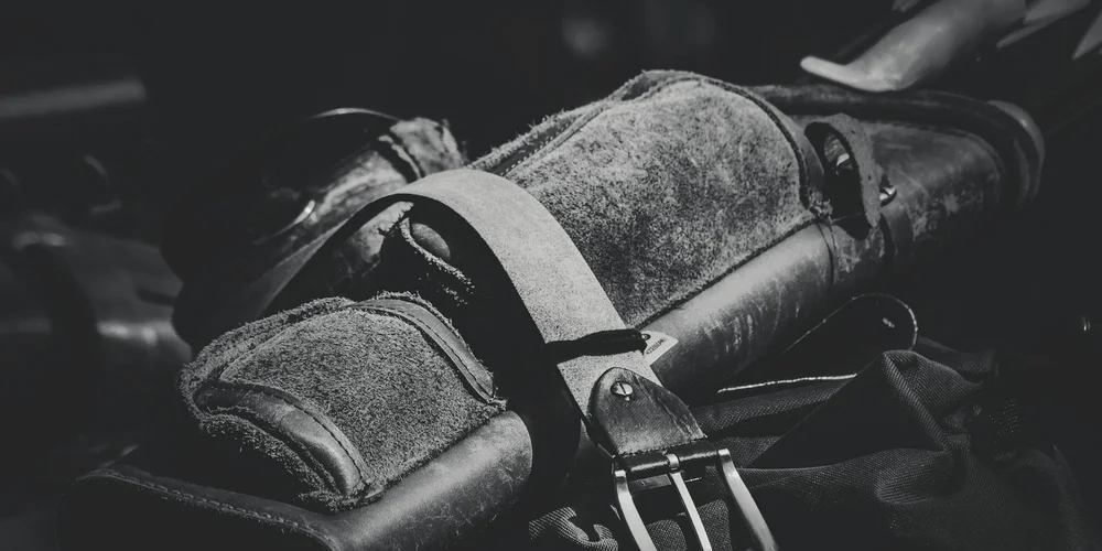 Black-and-white image of a textured leather bag with straps and buckles.