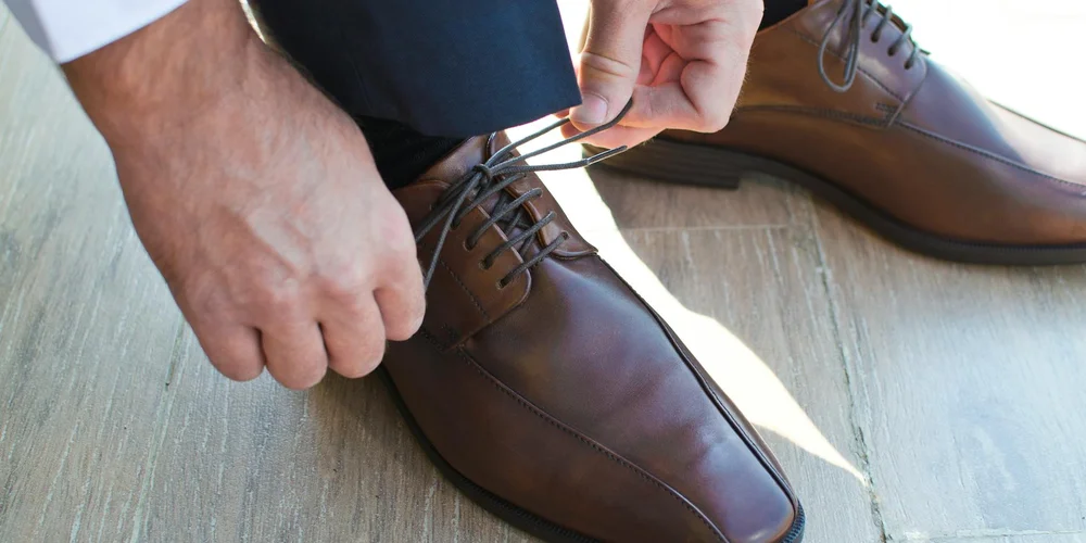 Close-up of hands tying brown leather dress shoes