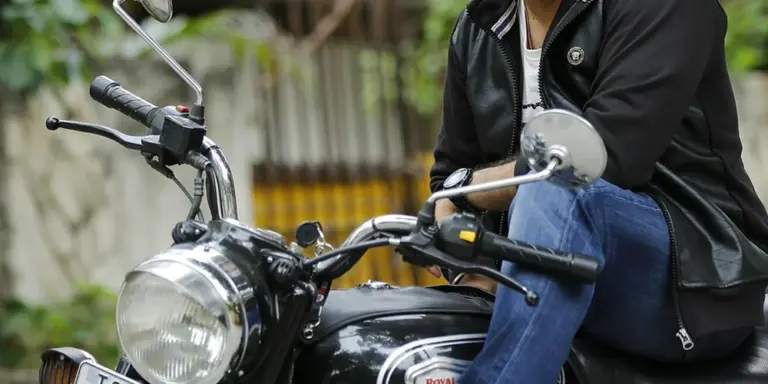 A person wearing a black leather jacket sits astride a motorcycle outdoors