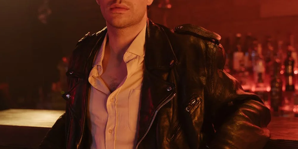 A person wearing a black leather jacket over a pale shirt in a dimly lit bar, illustrating versatile styling from casual to smart.