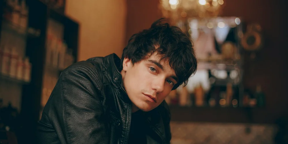 Person wearing a dark leather jacket indoors, looking at the camera.