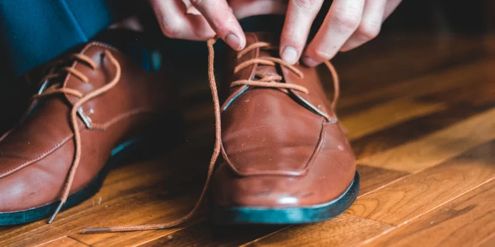 Close-up of hands tying brown leather laces on a pair of brown leather shoes