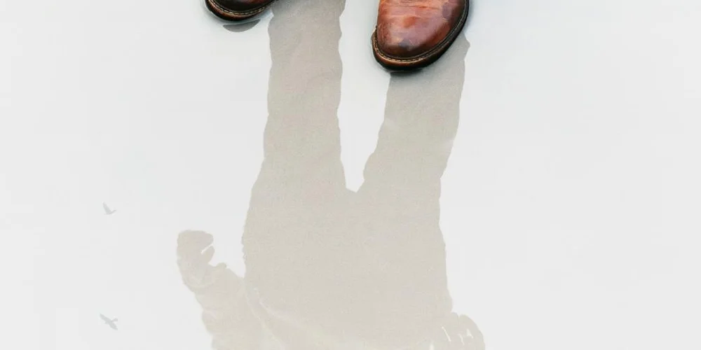 Top-down shot of two brown leather boots stepping onto a pale surface, with a water-streak trail forming beneath them.
