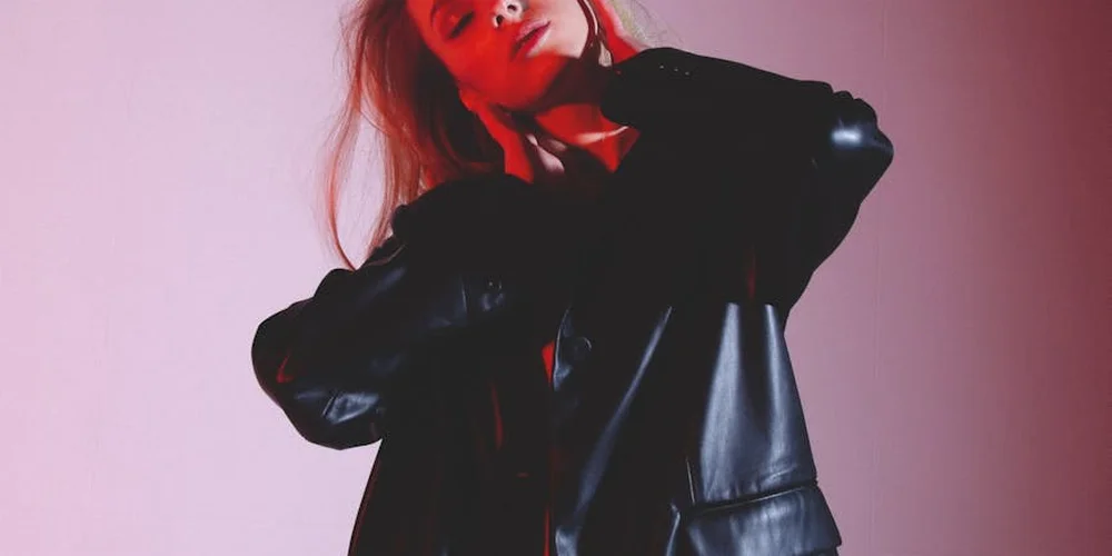 Person wearing a black leather jacket against a pink background.