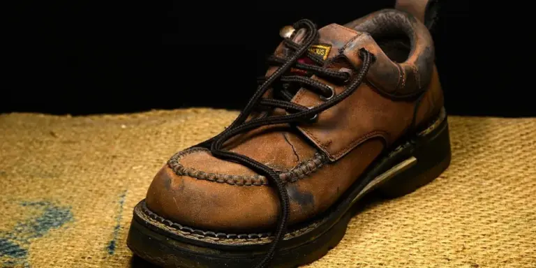 Brown leather footwear with laces on a textured woven surface.