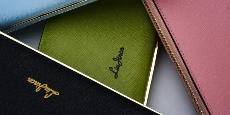 Colorful leather goods such as wallets and cases in blue, green, pink, and black with visible zippers and logos.