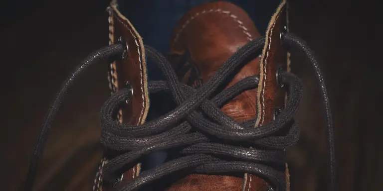 Close-up of a brown leather boot with dark laces, highlighting the leather texture and pores.