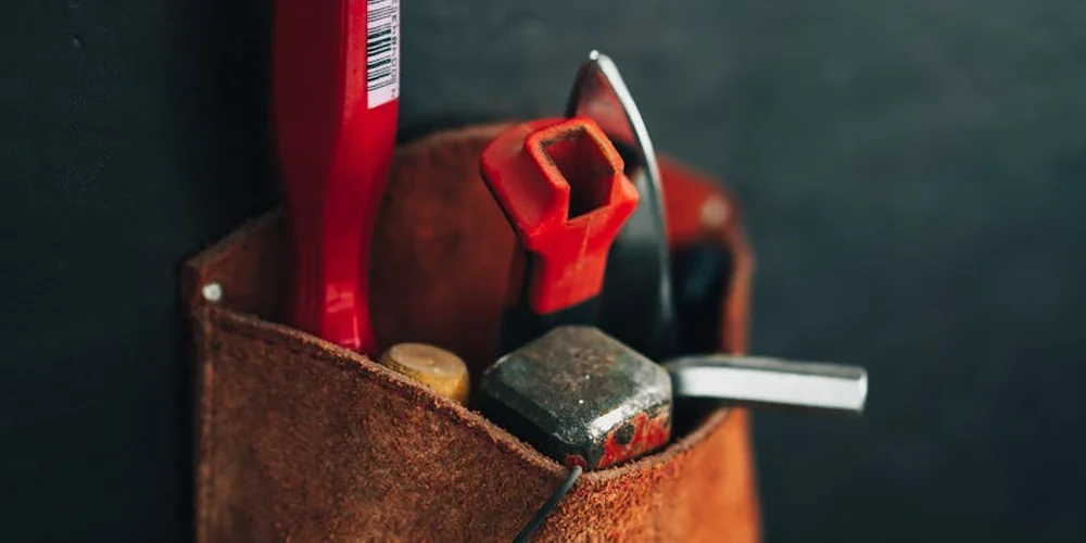 Close-up of leather repair tools in a brown leather pouch, including a red-handled tool and a small metal blade.