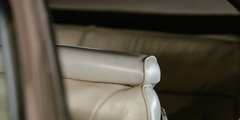 Close-up of a damaged beige leather car seat seam with exposed padding.