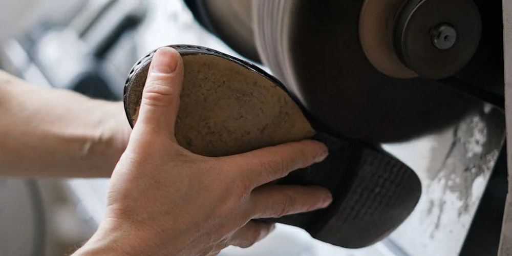 Close-up of hands holding a leather shoe near a rotating buffing wheel, preparing to remove scuffs and restore shine.