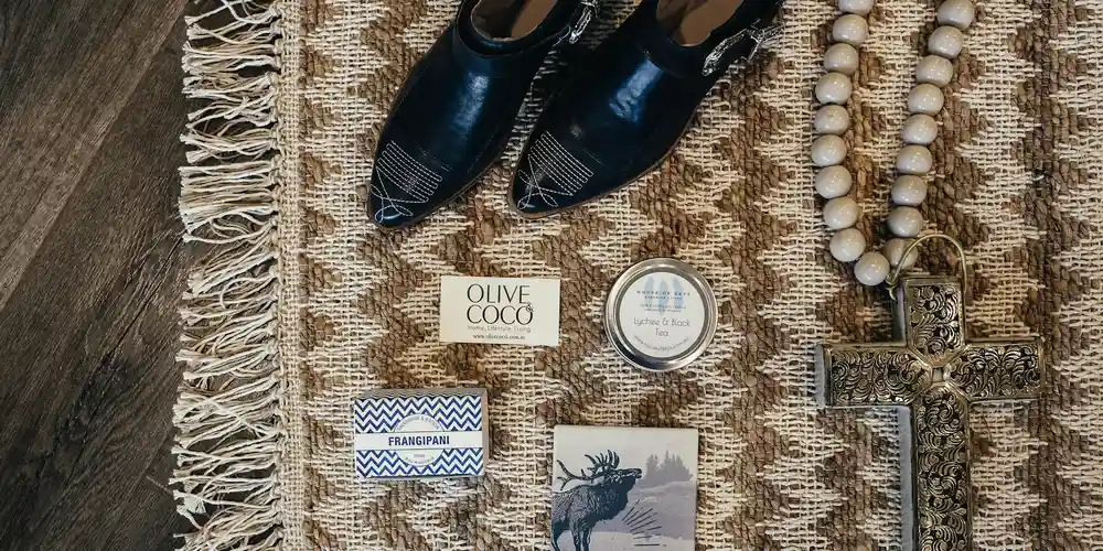 Black leather dress shoes on a woven rug surrounded by small boxes, a tin, and a beaded necklace, illustrating a setup for preventing glue damage on leather.
