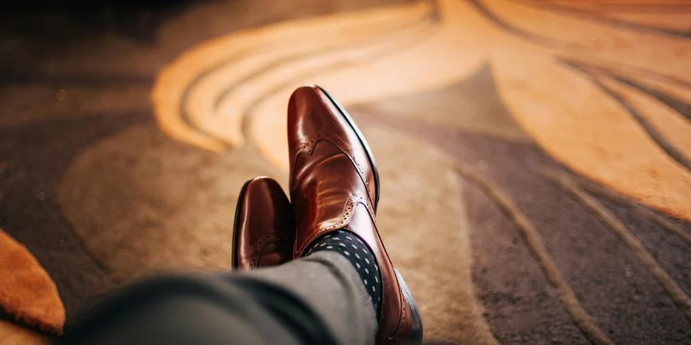 Close-up of polished brown leather dress shoes resting on a patterned carpet