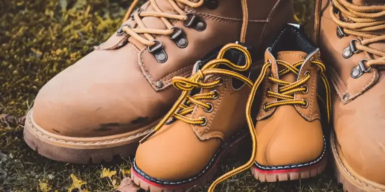 Close-up of tan leather boots with visible scuffs and scratches and yellow laces, resting on grass.