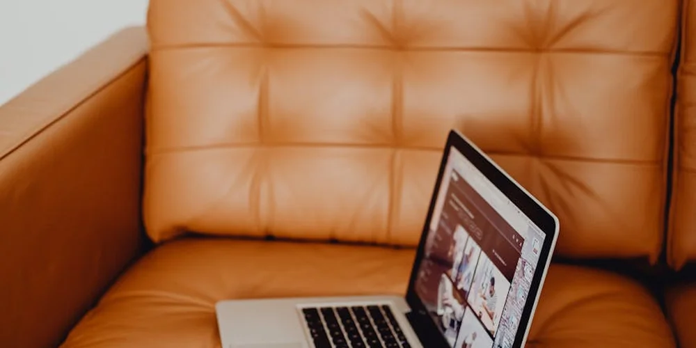 Tan leather sofa with tufted cushions and a laptop resting on the seat, illustrating a living room setup for leather repair guidance.