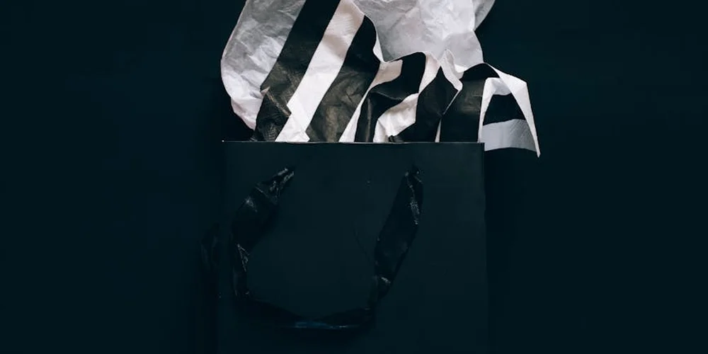Black shopping bag with white tissue paper featuring bold black stripes protruding from the top.