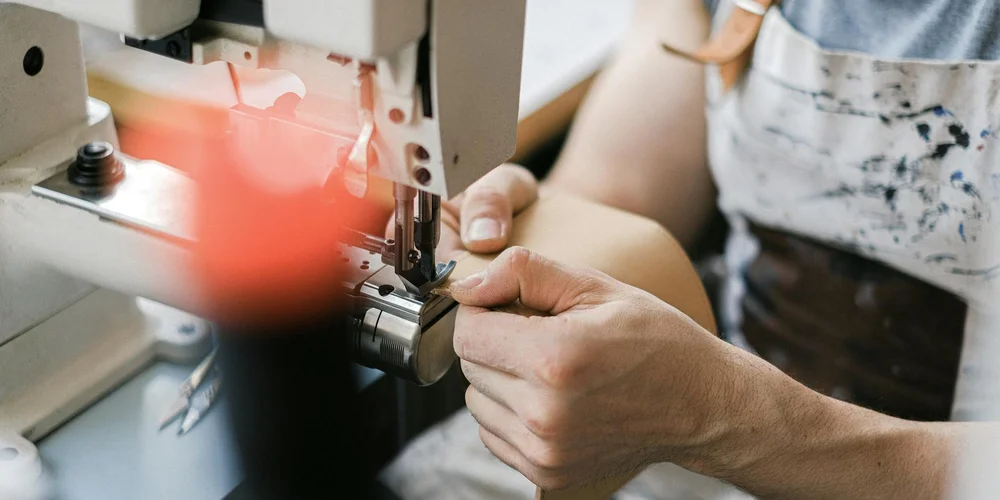 A craftsman’s hands guide a leather piece through a stamping/embossing machine to create texture.