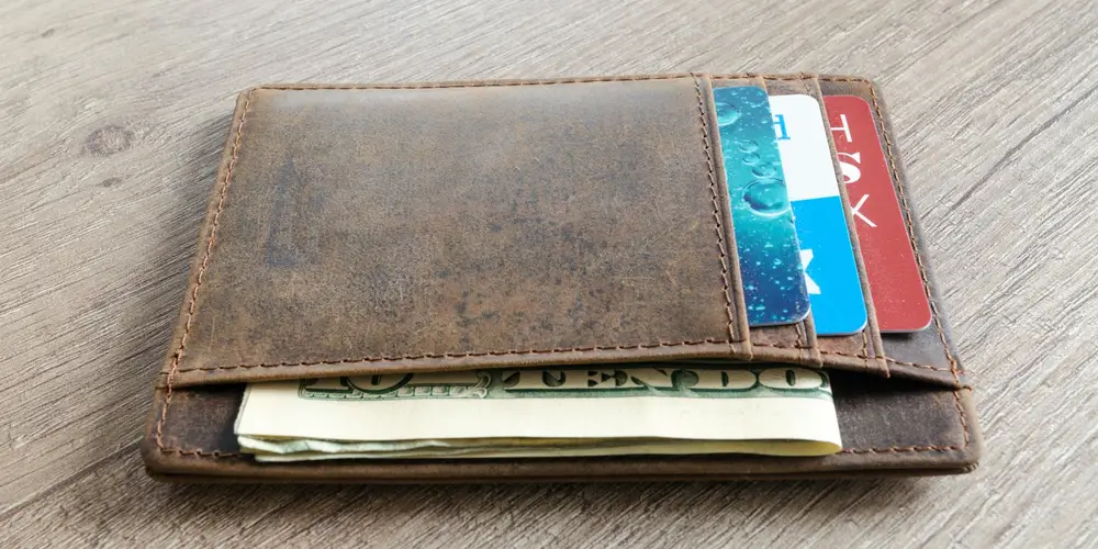 Brown leather wallet with cards and cash on a wooden surface