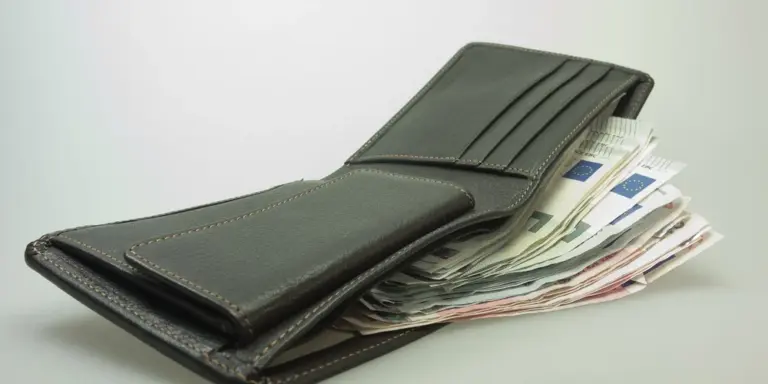 Dark leather wallet with cash partially visible on a light background.
