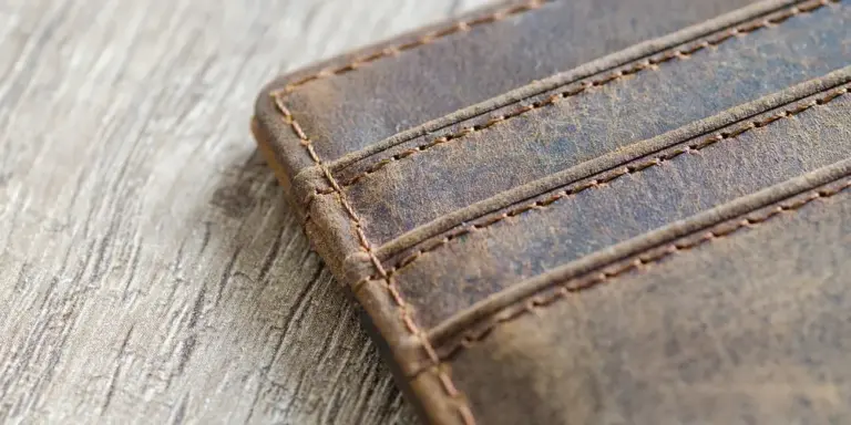 A close-up view of a brown leather wallet showing visible stitching and grain on a wooden surface.