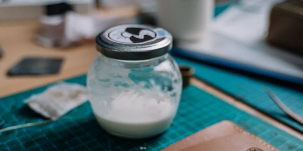 Jar of leather-care cream on a craft table with a green cutting mat in the background.