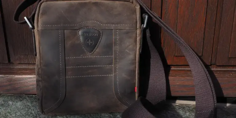 Brown leather bag with a shoulder strap on a wooden surface.