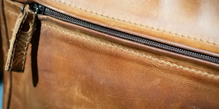 Close-up of a brown leather bag with a zipper and visible stitching.
